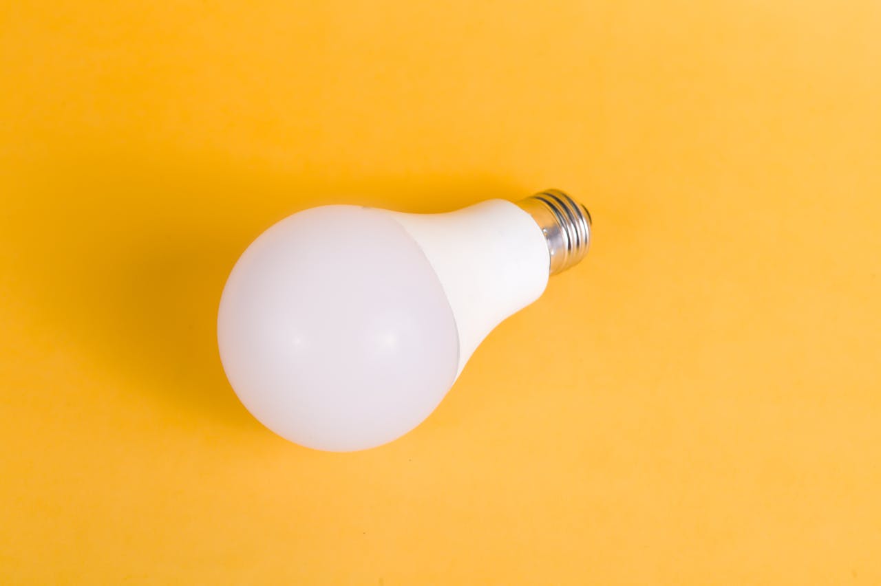 Minimalistic photo of a single LED light bulb against a bright yellow background for creative concepts.