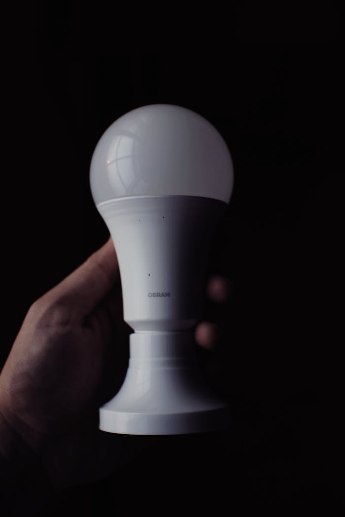 Hand gripping an LED light bulb against a dark backdrop for creative concepts.